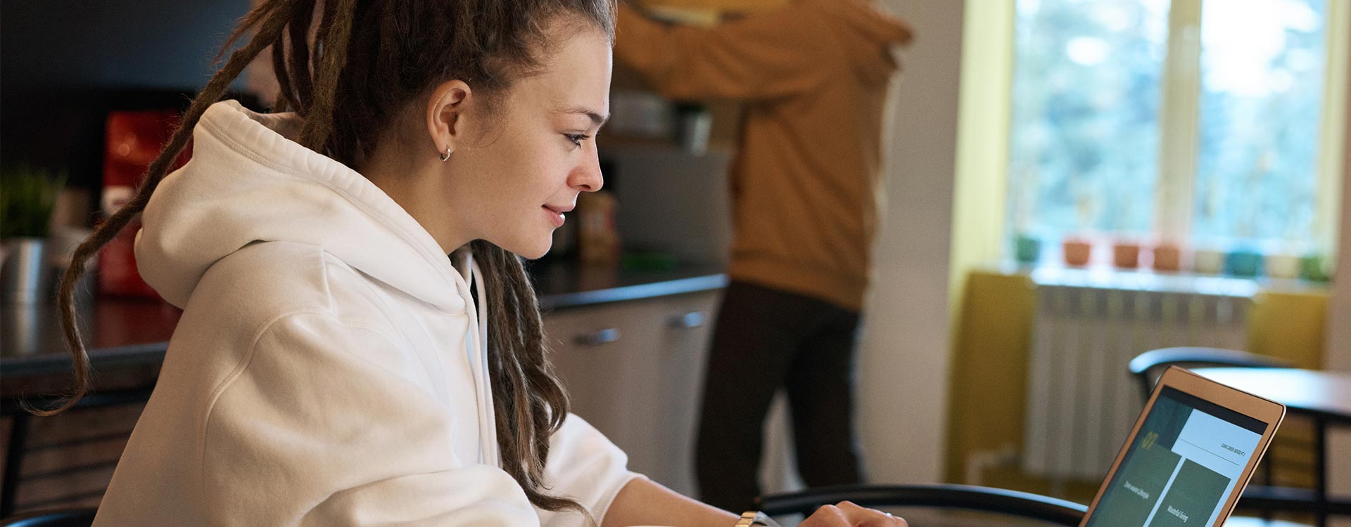 Mulher com dreadlocks desenvolve interface na mesa da cozinha: cena comum de quem quer trabalhar remoto a partir de casa