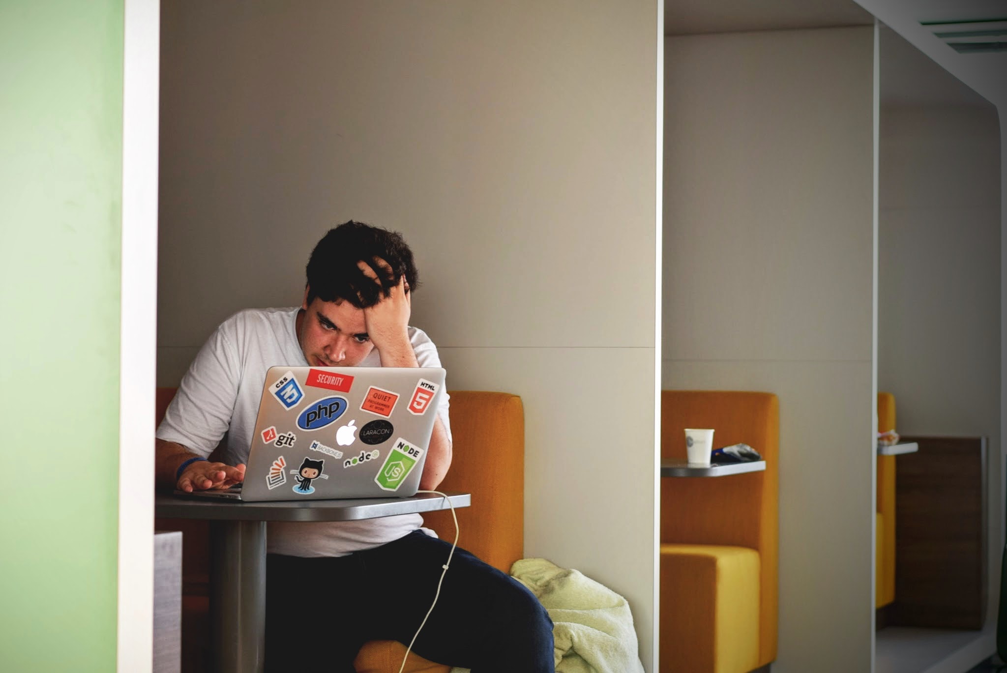 Young man in white shirt using his Macbook is looking at screen with a worried face