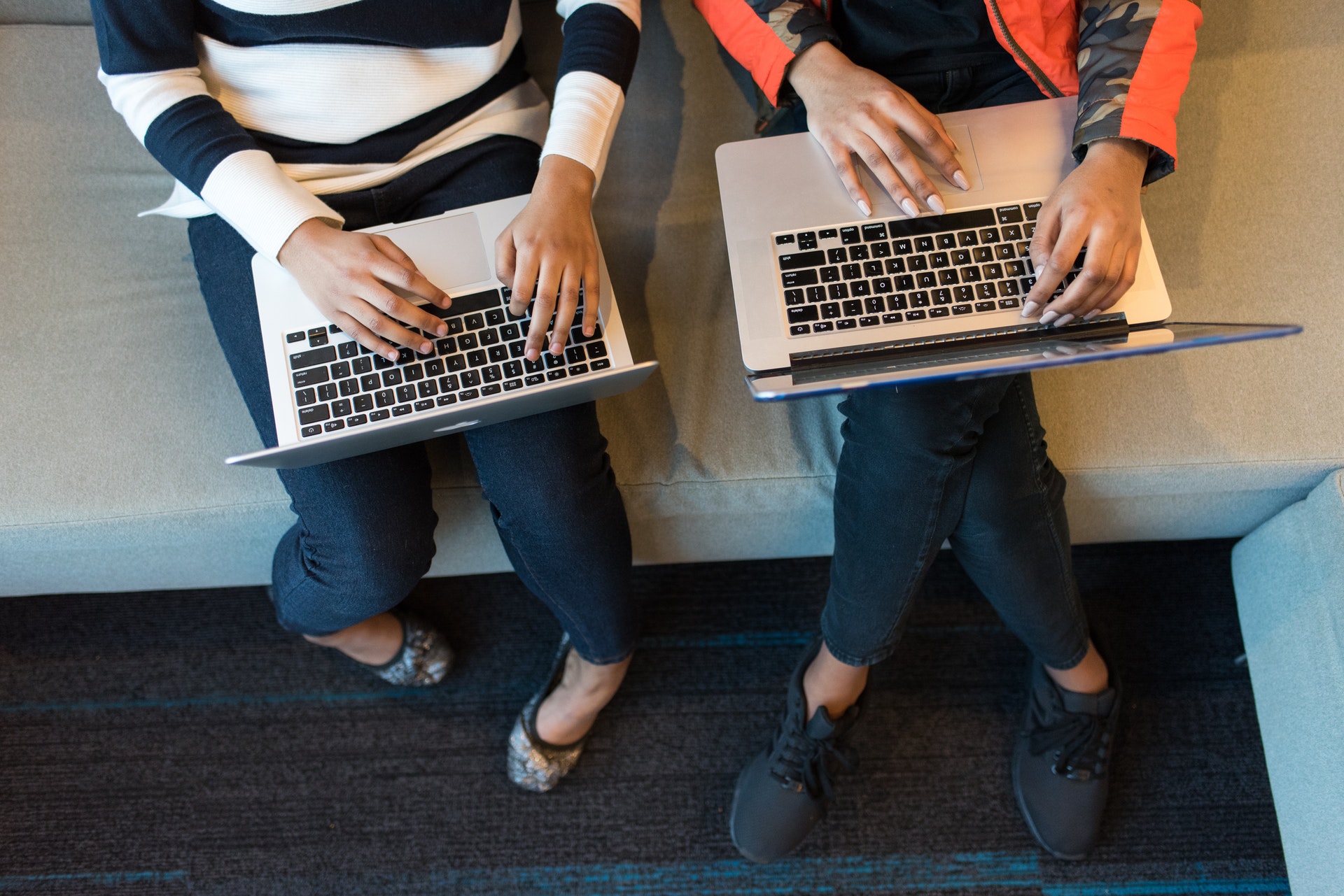 Two women sit side by side and work on their laptops