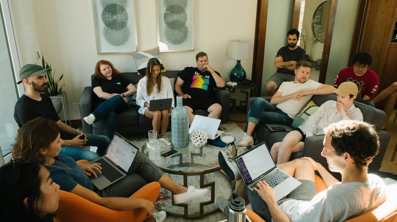 11 engineers sit together in a living room with notebooks on their laps, discussing how to improve their SDLC