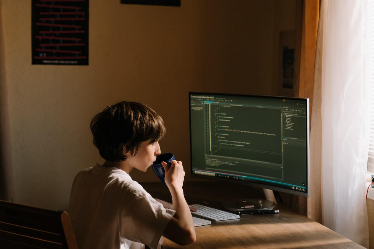 A common image in Distributed Teams for Software Development : boy in white tshirt drinks from mug while coding
