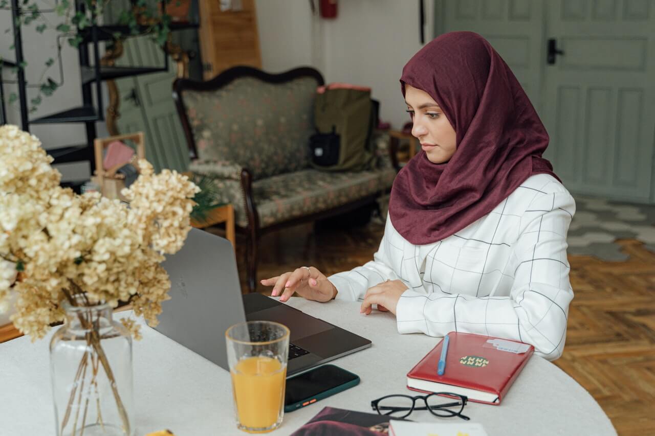 Woman wearing a hijab is sitting at home, working on the computer